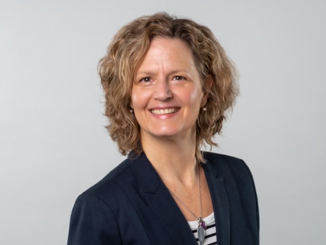 Frau Baumeister vor einem grauen Hintergrund, sie lächelt in die Kamera.