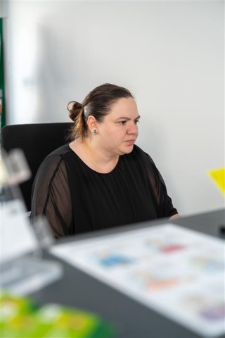 Die Mitarbeiterin Eva Eckstein sitzt hinter einem Tresen und guckt fokusiert auf etwas.