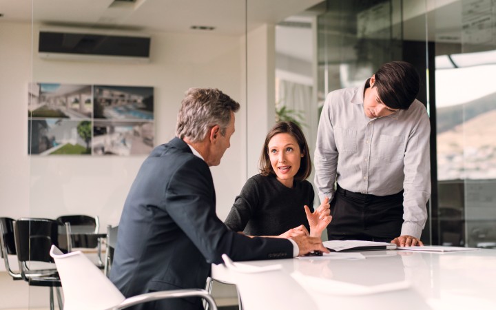 Kollegin und zwei Kollegen sitzen an einem Konferenztisch und sprechen über Dokumente auf dem Tisch