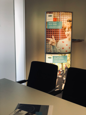 im Vordergrund steht ein Tisch mit shcwarzen Stühlen und dahinter steht ein HDI Ständer