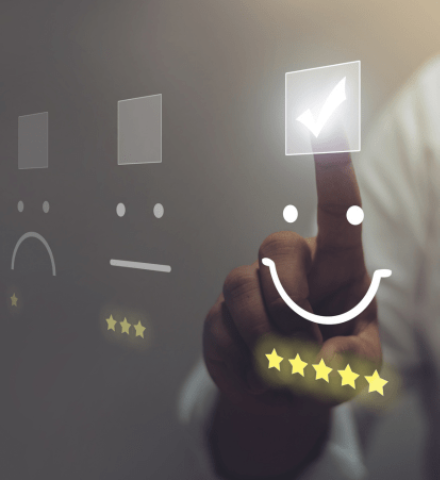 Auf dem Bild sind drei Smileys zusehen, ein lachender, ein neutraler, ein unzufriedener. Dahinter eine Hand die auf den zufriedenen Smiley zeigt und ihn ankreuzt, das Bild soll für die Kundenzufriedenheit stehen