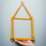 Haus aus einem Holzstockund unter diesem Haus befindet sich eine Hand, die das Haus hält. 