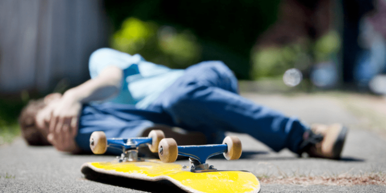 Mann liegt am Boden und hält sich das Knie. Vor him leigt ein gelbes Skateboard.