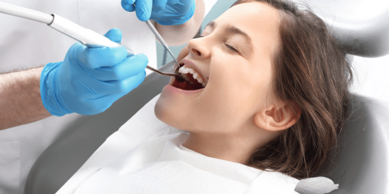 Ein Mädchen liegt aus einem Stuhl und hat den Mund auf. Da Ihre Zähne mit medizinischen Instrumenten untersucht werden. 