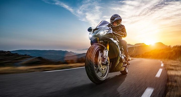 Ein Motorradfahrer fährt auf einer Straße und hinter einem Berg geht die Sonne unter.