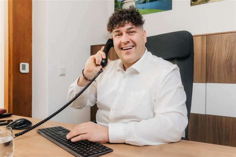 Schneider sitzt am Schreibtisch und hält den Höher vom Telefon an sein rechtes Ohr.