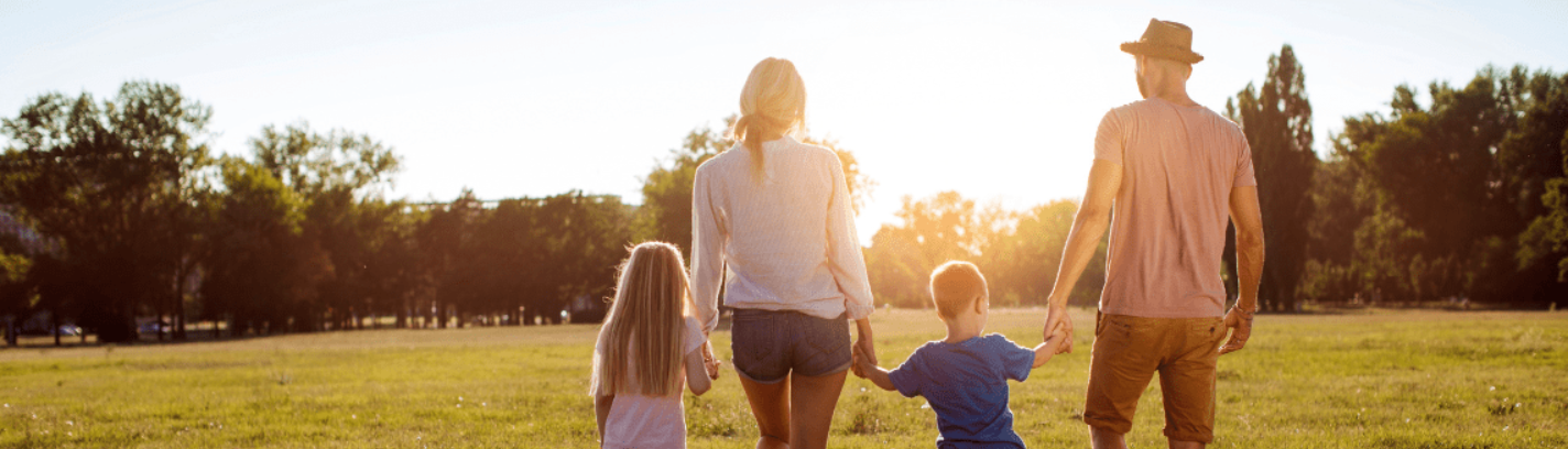 Ein kleine Familie ist rechts vom Bild. Familie von rechts nach links: ein kleines Mädchen, die Mutter, ein kleiner Junge und der Vater. Sie gehen auf einer Wiese in Richtung Wald und die Sonne geht unter.