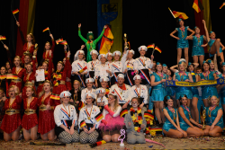 Vielen Menschen, drei verschiedene Gruppen feiern die Siegerehrung. Die Gruppe links hat rote kurze Kleider an. Die Gruppe in der Mitte ist als Köche verkleidet. Die Gruppe rechts hat blaue Kleider an. 