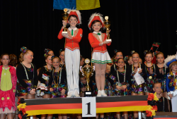 Ein Mädchen und ein Junge stehen auf dem ersten Platz mit jeweils einem Pokal. Dahinter stehen weiter Menschen mit Medallien. 