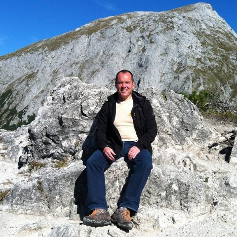 Frank Türkowsky sitzt auf einem grauen Stein. Hinter Ihm ist  ein Teil eines grauen Bergs.
