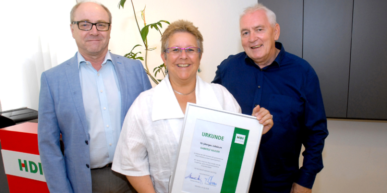 Mitarbeiter foto in einem Büro, in der Mitte steht Gabriele Haaser mit der 10 jährigen Urkunde