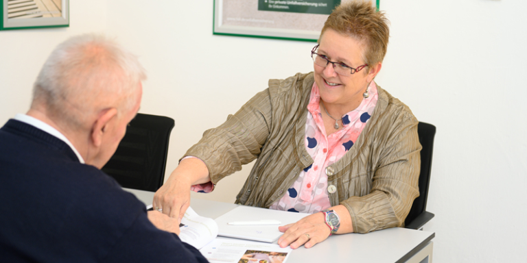 Gabriele Haaser sitzt an einem Schreibtisch und erklärt einem Mitarbeiter etwasin einer Zeitung