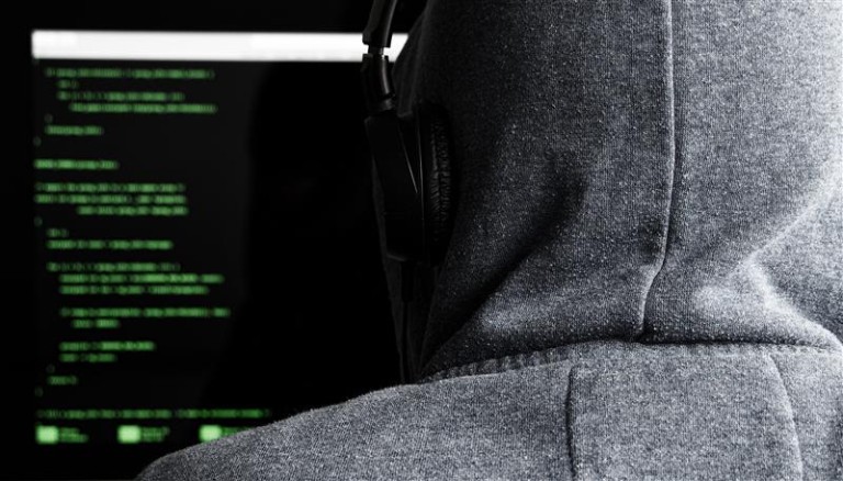 Mann mit einem Hoodie und Kopfhöher, den man von hinten sieht, gzckt auf einen Bildschirm mit Daten 