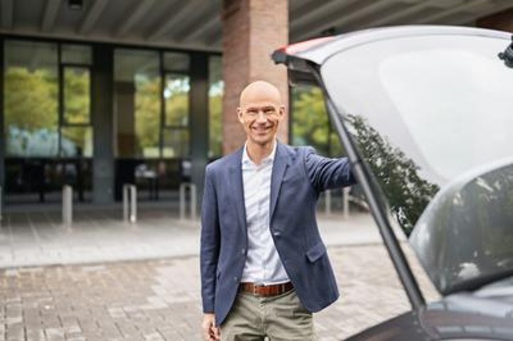 Ein Mann, der in die Kamera lächelt, steht am Kofferraum eines Autos