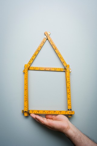 Haus aus einem Holzstockund unter diesem Haus befindet sich eine Hand, die das Haus hält. 