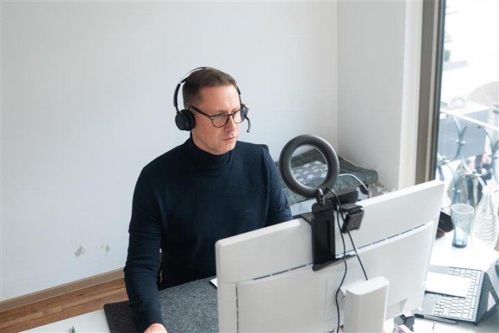 Scheffler sitzt an einem Schreibtisch und guckt auf einen PC, dabei hat er ein Headset auf dem Kopf.