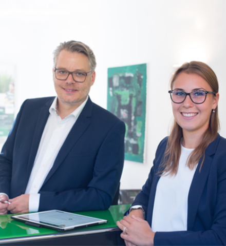Jan Georg Weyers und Laura Marie Heidschuster stehen gemeinsam am Empfangstresen, zwischen ihnen liegt ein Tablet