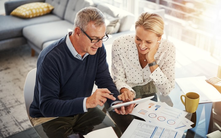 Paar das auf Tablet guckt und Dokumente mit Grafiken und Tabellen vor sich ausgebreitet hat