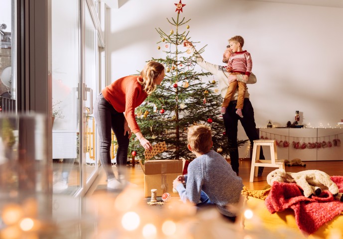In der Mitte steht ein Weihnachtsbaum und drumherum ist eine Familie, die den Baum schmückt.