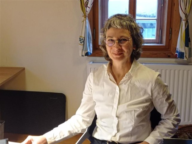 Kristina Ramm sitzt am Schreibtisch und lächelt in die Kamera.