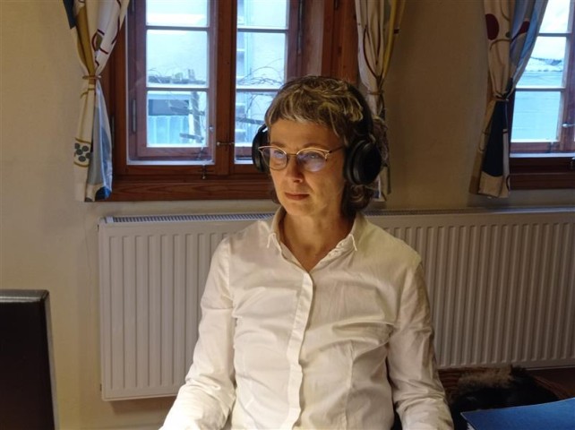 Kristina Ramm sitzt mit Kopfhörern am Schreibtisch und sie guckt konzentreirt nach unten.