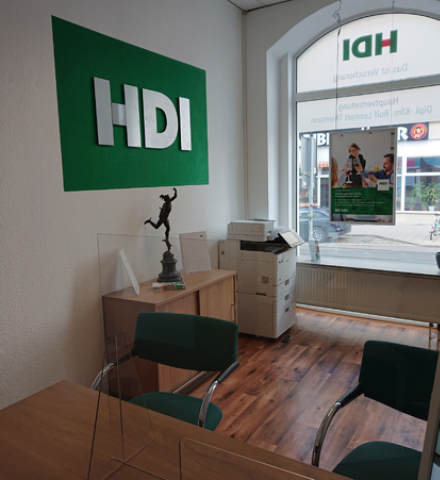 Beratungsbereich für Kunden in der Agentur. Zwei Stühle stehen vor einem Schreibtisch, an der Wand befindet sich das HDI Logo und im Hintergrund kann man durch das Schaufenster nach draußen sehen.