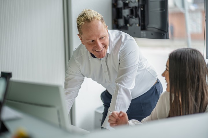 Marcus Berg steht an einem PC und lächelt dabei eine Mitarbeiterin an. 
