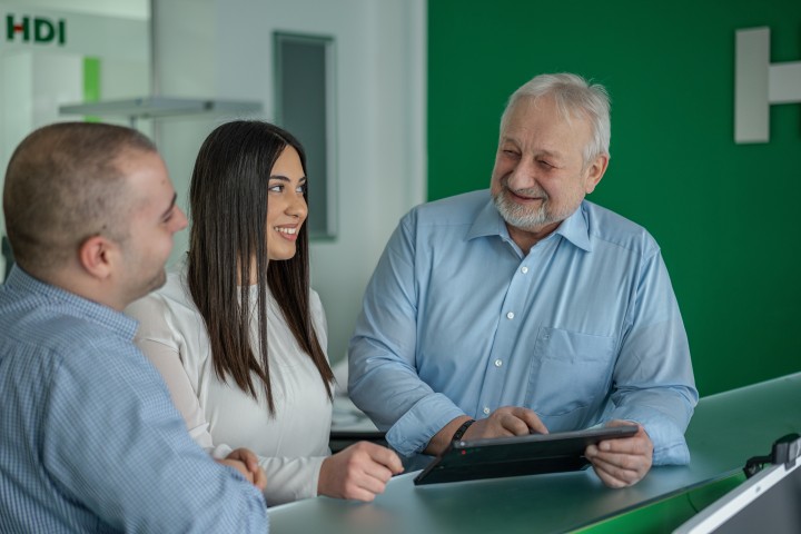 Drei Mitarbeiter stehen an der Theke. Der Mitarbeiter rechts außen hat ein Ipad in der Hand und zeigt etwas auf dem Gerät. Dabei lächeln sich alle drei Mitarbeiter an. 