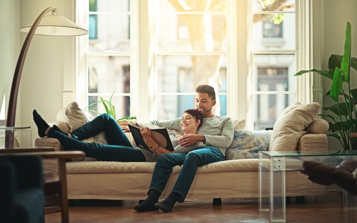 Paar, das zusammen auf der Couch liegt und in einem Buch liest.