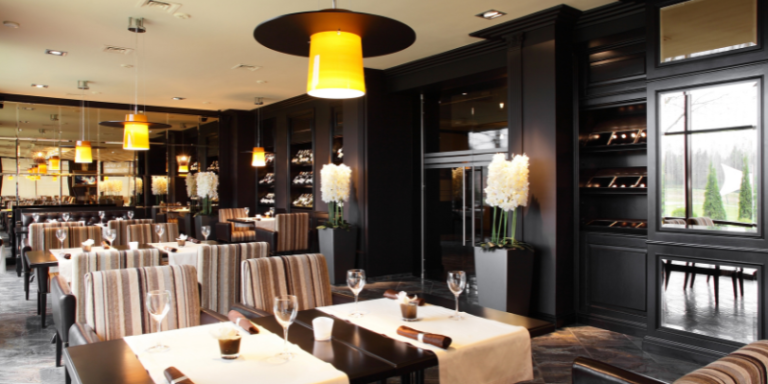 Innenraum einer Gastronomie mit Tischen, Stühlen, Lampen und schwarzen Wänden