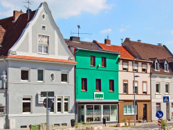 grünes Haus mit HDI Logo, Fenster und unten ist eine Fensterfront, links neben der Agentur steht ein graues Haus und rechts neben der Agentur steht ein rosa, braunes Haus