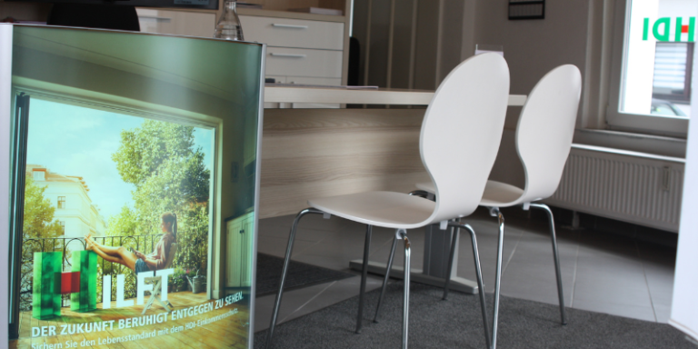 Man sieht einen Schreibtisch vpr dem zwei Stühle stehen, im Vordergrund sieht man einen Werbeaufsteller von HDI