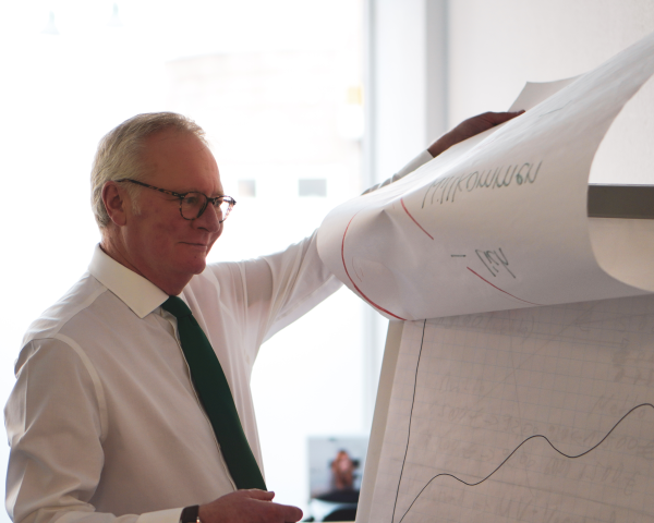 Michael Jansweid der gerade die nächste Seite auf einem Flipchart umblättert. Auf dem Flipchart sind Zeichnungen von Diagrammen und Grafiken.