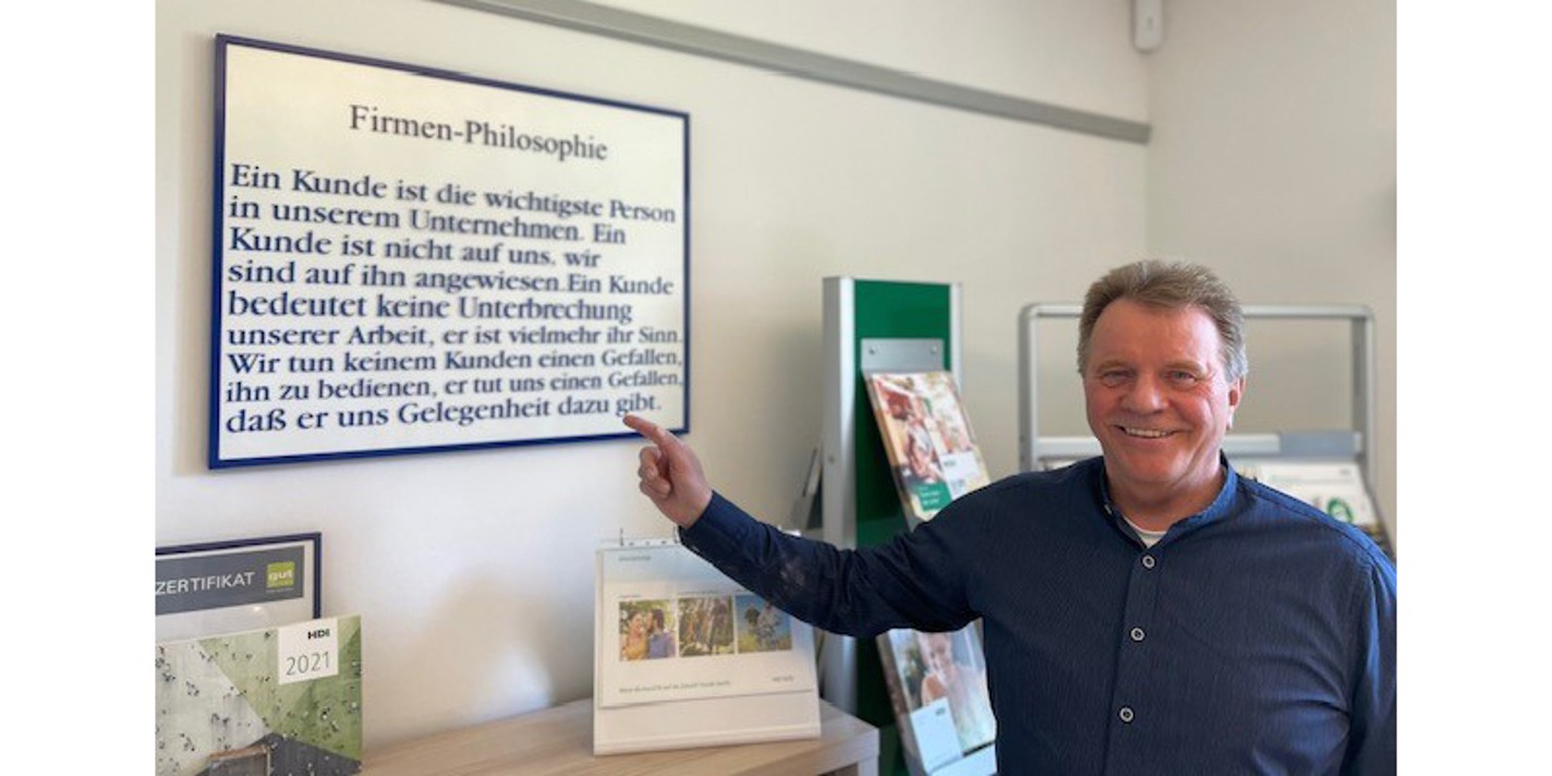 Norbert Redöhl steht in seiner Agentur und zeigt auf ein Plakat, auf dem die Firmenphilosophie steht. 
