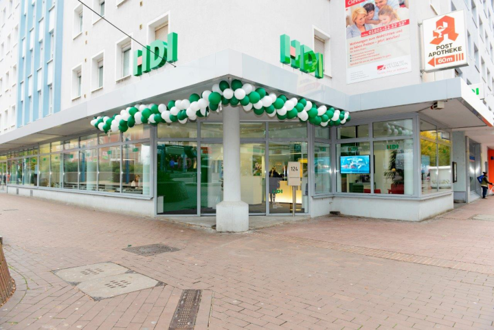 Man guckt von der Straße auf ein Hochhaus, im Erdgeschoss befindet sich die HDI Agentur, das Vordach ist mit grünen und weißen Luftballons geschmückt, durch viele bodentiefe Fenster erhält mein einen Blick auf die Innenräume der Agentur