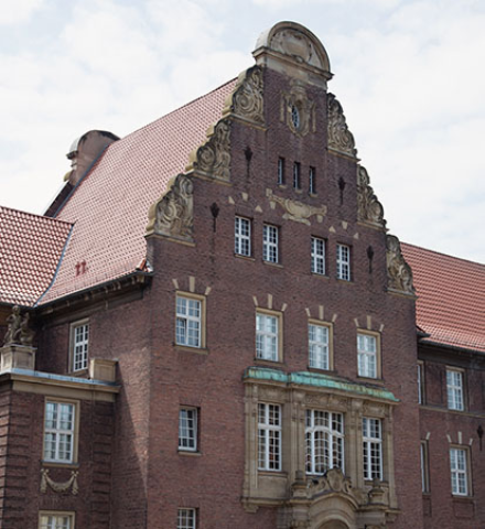 rotes Steingebäude mit goldenen Details und rotem Dach und ein blau, weißer Himmel ist zu sehen.