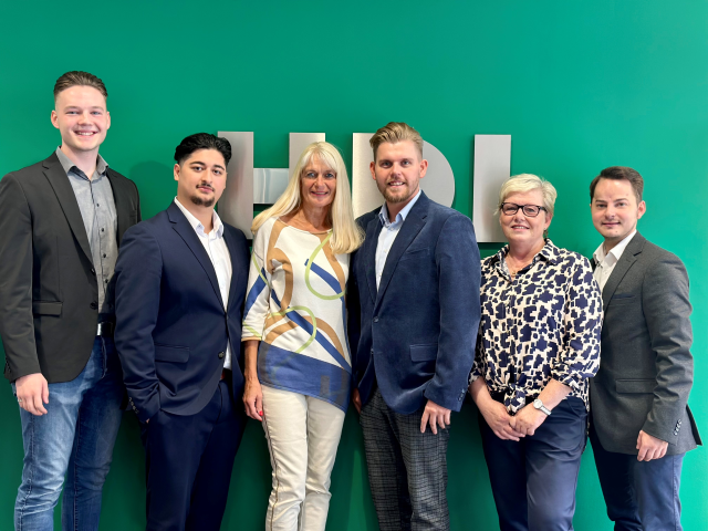 Sechs Mitarbeiter stehen in einer Reihe an einer grünen Wand mit dem silbernen HDI Logo, das durch die Mitarbeoiter verdeckt wird.