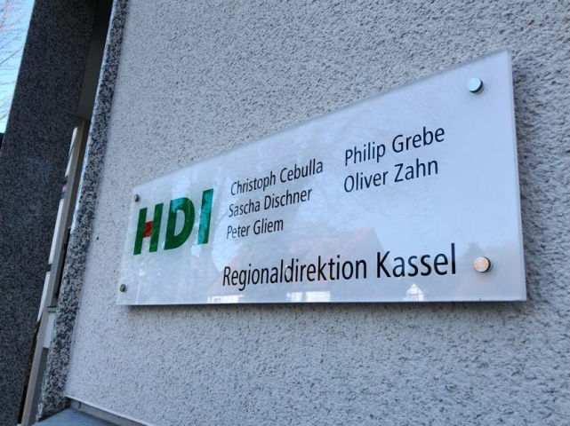 HDI Schild an der Hauswand, links ist das HDI Logo, daneben stehen Namen´, wie Christoph cebulla, Philip Grebe, Sascha Dischner, Oliver zahn und Peter Gliem. darunter steht Regionaldirektion Kassel