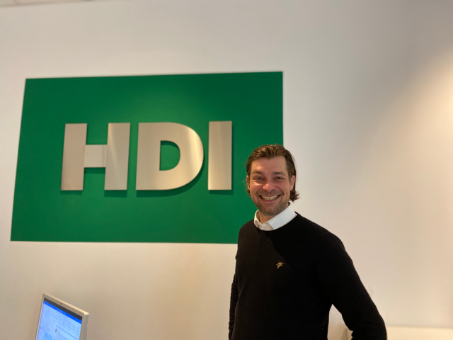 Mitarbeiter Philipp Meincke vor einer grünen Wand mit silber HDI Logo