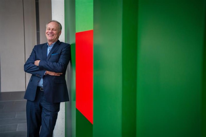 Rainer Ernst lehnt lachend an dem grünen H vom HDI Logo.