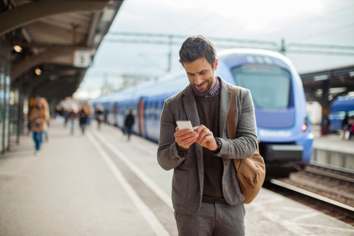 Mann der an Bahnsteig wartet und auf sein Handy schaut