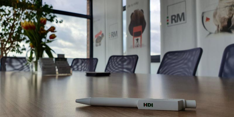 Büroinneraum - im Fokus ist ein weißer Kugelschreiber mit dem HDI Logo, der auf einem Konferenztisch liegt.