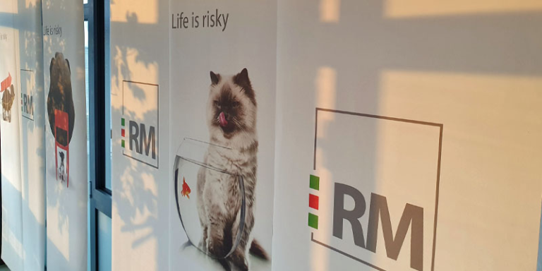 Stoffbanner. Darauf abgebildet sind das Logo der HDI Generalvertretung RM Risk Management, der Schriftzug "Life is risky" und eine Katze die sich das Maul leckt und vor einem Goldfischglas sitzt.