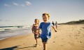 Lachende Kinder die am Strand langrennen