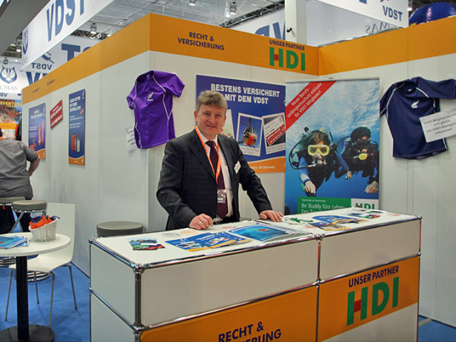 Man sieht Stefan Dröfler der an einem Tresen steht. Auf dem Tresen steht "Unser Partner HDI". Der Tresen ist Teil eines Standes auf einer Infoveranstaltung des VDST.