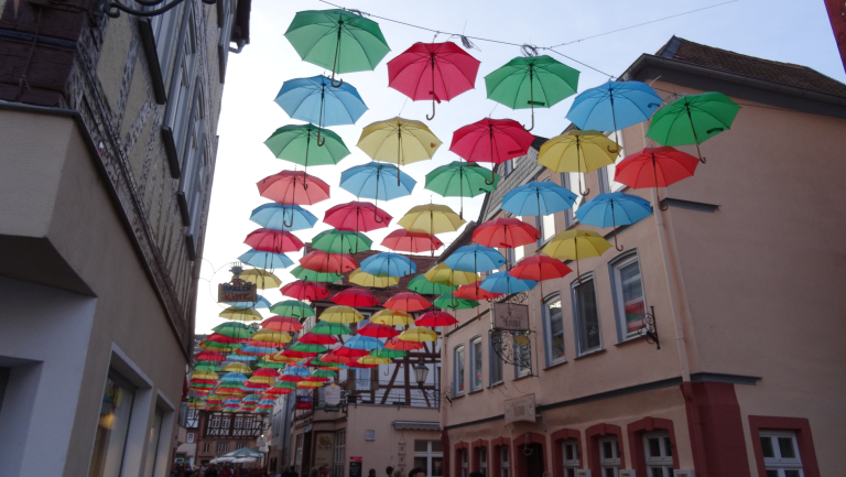 Man sieht eine Gasse, über der Gasse befindet sich eine Konstruktion aus bunten, aneinander gereihten Regenschirmen