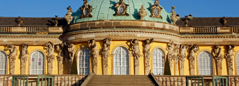 gelbes Schloss mit türkisem dach, Fenster und braune Statue. vor dem Schloss ist eine Treppe