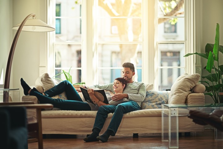 Paar, das zusammen auf der Couch liegt und in einem Buch liest.