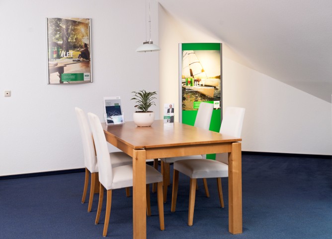 Man sieht einen Tisch mit vier Stühlen. Auf dem Tisch steht eine Pflanze, sowie zwei Aufsteller mit Infobroschüren. An der Wand hängt eine Werbeposter von HDI. Hinter dem Tisch steht ein Leuchtaufsteller von HDI.