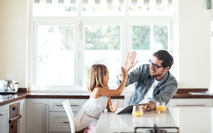Vater und Tochter in der Küche, beide lachen und geben sich ein High-Five